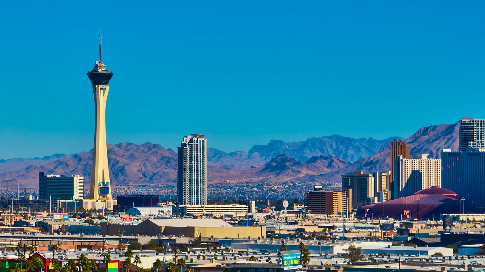 The STRAT tower and downtown Las Vegas buildings against desert mountains under a clear blue sky